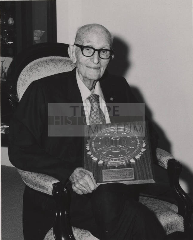 Carl Hayden seated holding large commemorative plaque.