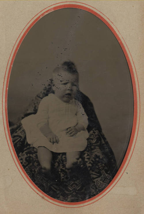 Unknown baby in a chair with a tapestry drape