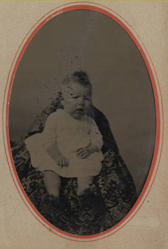 Unknown baby in a chair with a tapestry drape