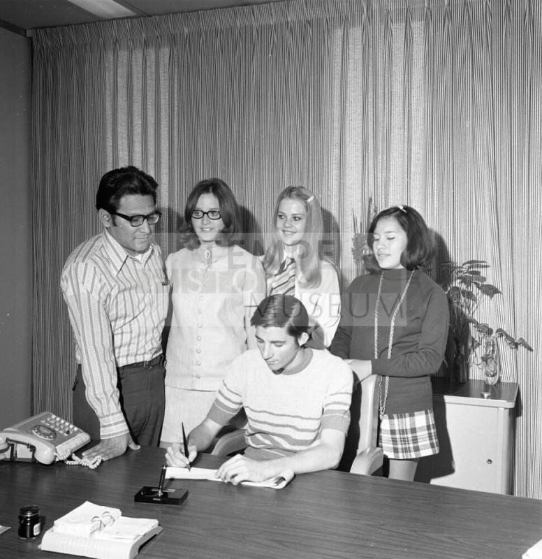 Man and 4 young people, one signing paper