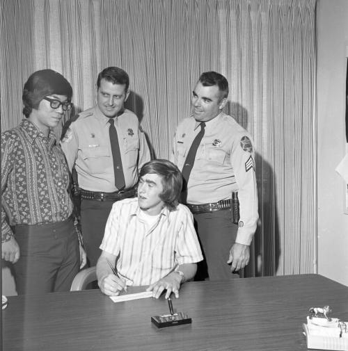 Two Police Officers and Teenage Boy at paper signing