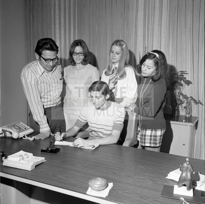 Four people watch teen sign paper