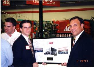 Photograph - 2 Men holding framed photos at the Grand Opening of Ace Hardware