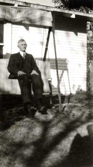 A Raymond Man sitting on a swing outside of a house