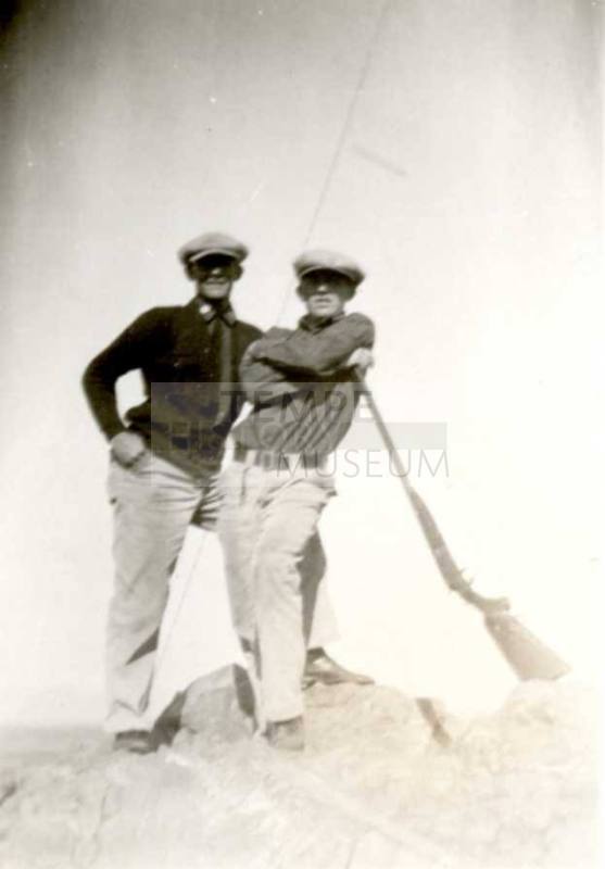 Frank Raymond and John stand with long rifles atop rocks