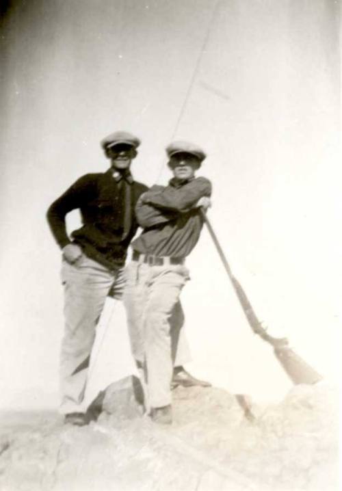 Frank Raymond and John stand with long rifles atop rocks