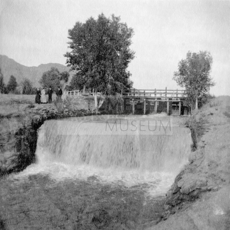 People standing by canal with waterfall and gates.