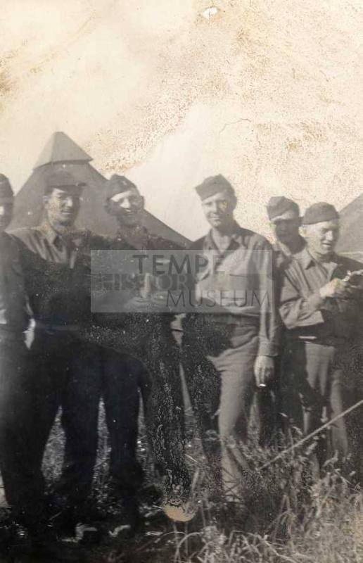 Photograph of six military personnel at a campsite