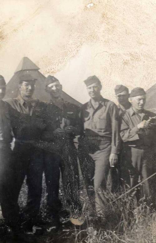 Photograph of six military personnel at a campsite