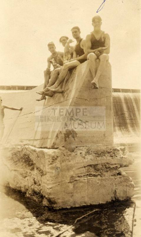 Four men in bathing suits sit on a concrete part of Granite Reef Dam