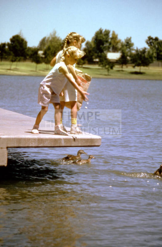 Two children feeding duck at Kiwanis Park lake - Mill & All American Way