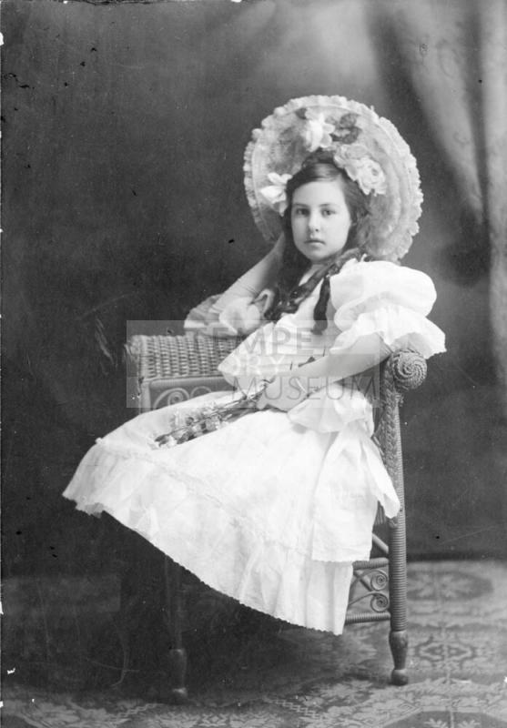Individual portrait of a preteen Mildred Muriel Hart seated in wicker chair