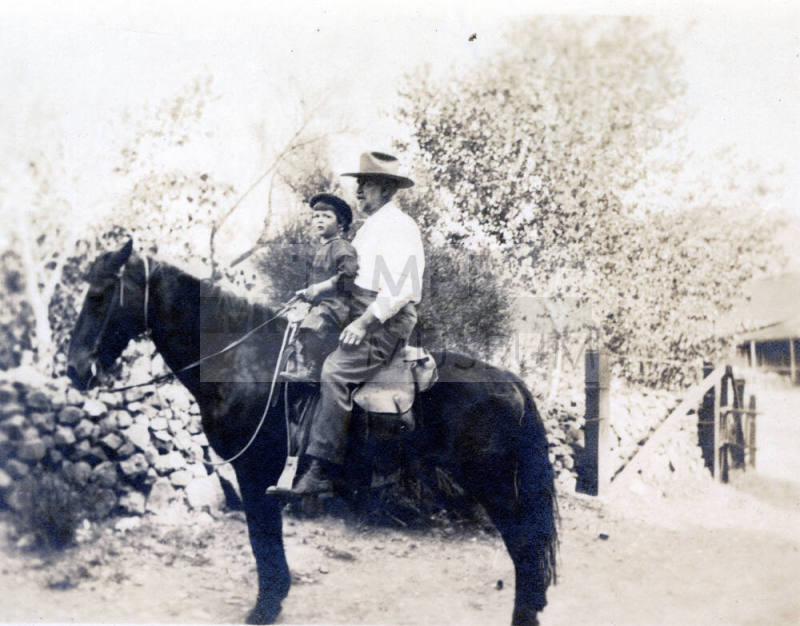Dr. Fenn J Hart atop a dark horse with small child named Bobby