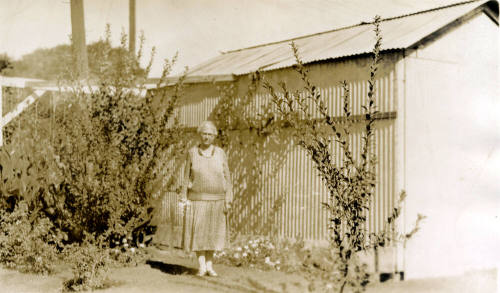 Rosa Brown Hart, wife of Dr. Fenn J Hart, standing in front of a shed outside their home in Phoenix