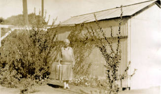 Rosa Brown Hart, wife of Dr. Fenn J Hart, standing in front of a shed outside their home in Phoenix