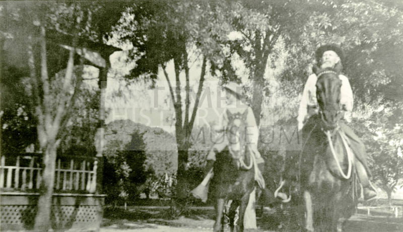 A man and a boy ride horses in front of Petersen house