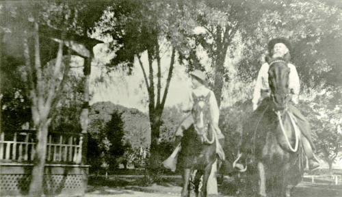 A man and a boy ride horses in front of Petersen house