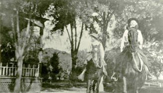 A man and a boy ride horses in front of Petersen house