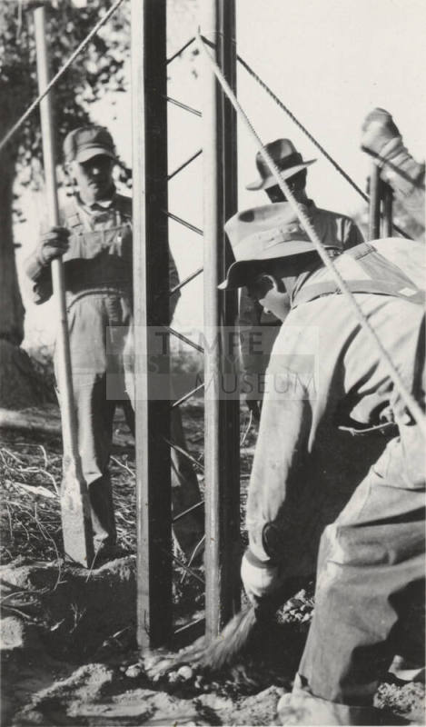 Man pouring cement at the base of steel poles