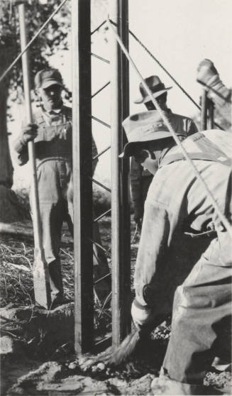 Man pouring cement at the base of steel poles