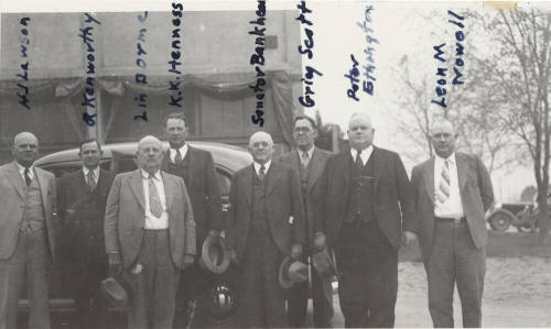 Photo- View of a identified group of eight men in front of a car and building