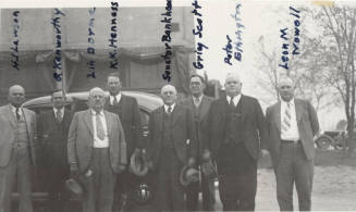 Photo- View of a identified group of eight men in front of a car and building