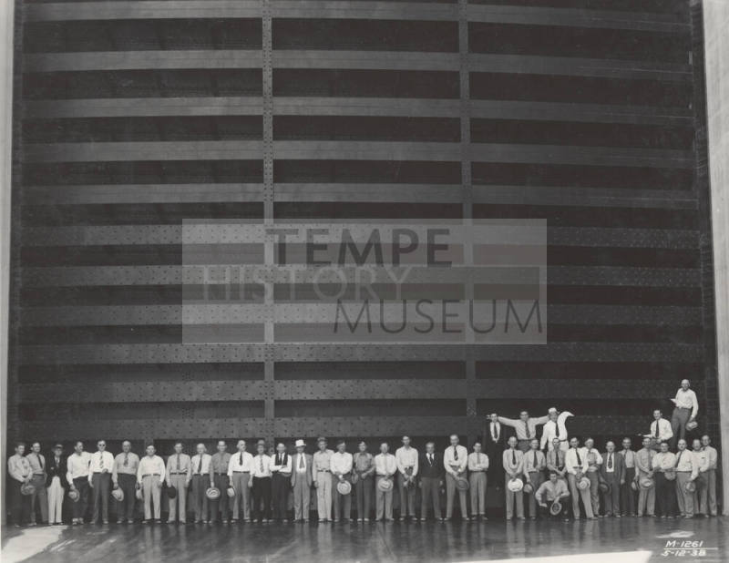 Photo- A row of forty men standing in front of spillway gate at Horse Mesa Dam