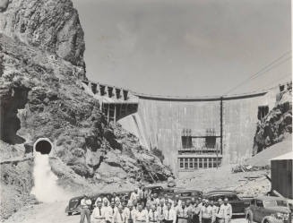 Photo- A row of thirty six men standing in front of Horse Mesa Dam with cars