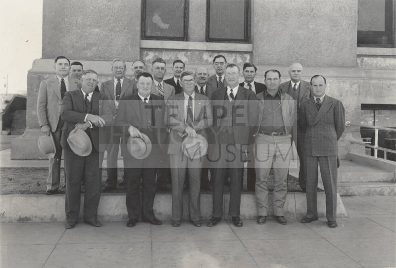 Photo- View of sixteen unidentified men standing in front of a building