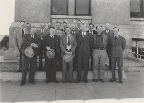 Photo- View of sixteen unidentified men standing in front of a building