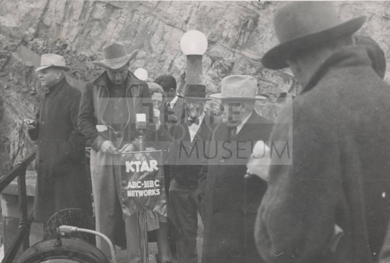 Photo-Group of people standing around a KTAR microphone at Roosevelt Dam