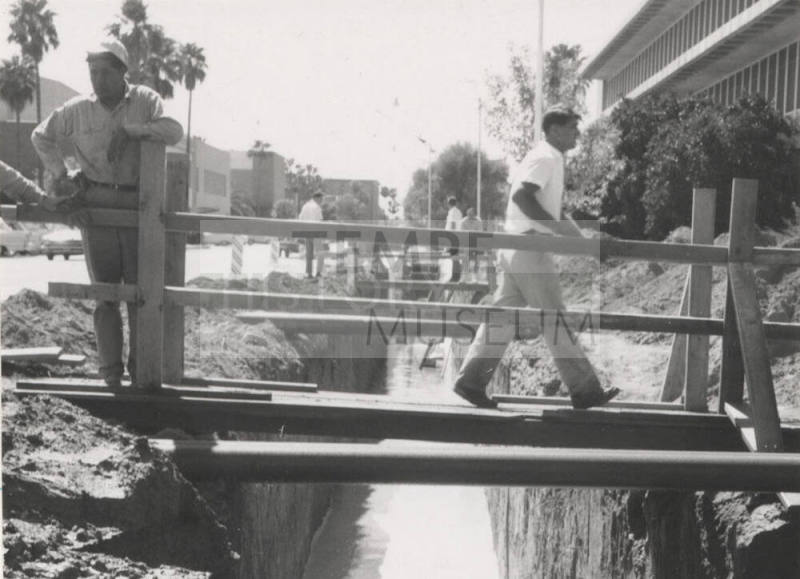 Construction men walking across footbridge over canal at Arizona State University
