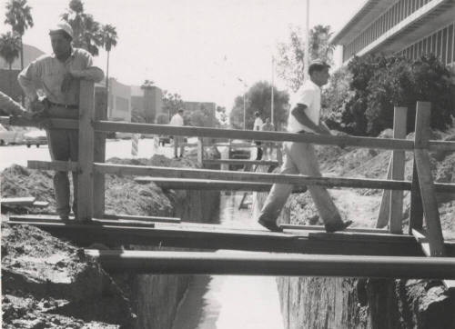 Construction men walking across footbridge over canal at Arizona State University