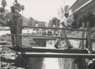 Construction men walking across footbridge over canal at Arizona State University