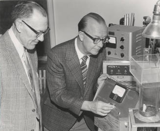 Dr. John Decker demonstrates his photosynthesis measuring device to Dr. Ira Judd